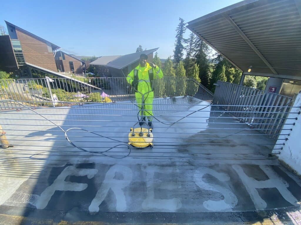 Fresh Family technician pressure washing the UW Bothell parking garage roof deck with a commercial surface cleaner