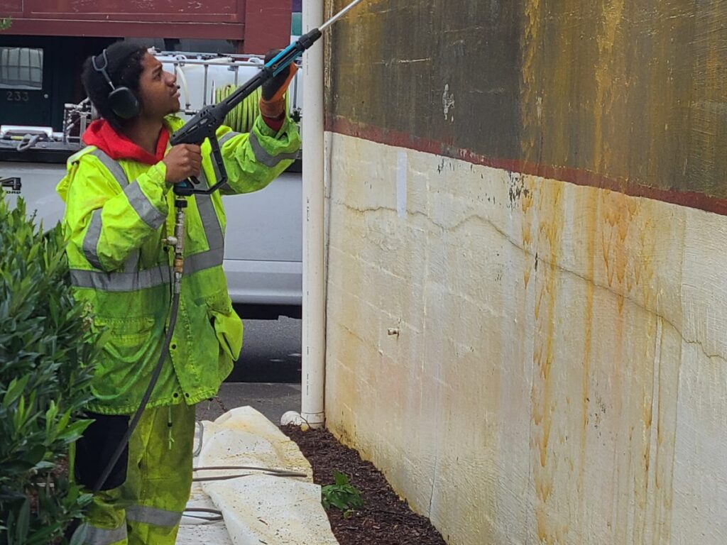 Crew member power washing a building wall in downtown Renton